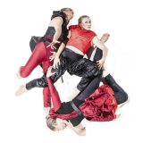 Kolme tanssijaa makaa vääntyneissä asennoissa kasassa. heidän vaatteensa ovat puna-mustat.